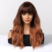A realistic female mannequin head displays a long, wavy DWY wig with a dark brown to copper red ombre color and stylish full bangs, against a clean white background.