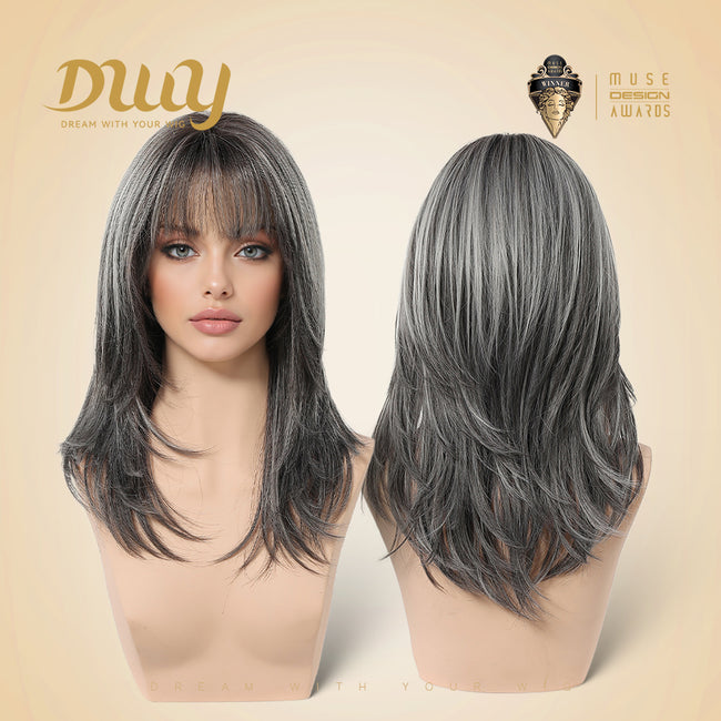 A split-screen studio product photo showing a realistic female mannequin head modeling a medium-length, layered synthetic wig in a salt-and-pepper grey color. The left view displays the frontal presentation with face-framing bangs and flipped layers. The right view shows the back of the wig, highlighting the texture and layered cut. The background is cream with the 'Duuy' and 'Muse Design Awards' logos.
