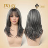 A split-screen studio product photo showing a realistic female mannequin head modeling a medium-length, layered synthetic wig in a salt-and-pepper grey color. The left view displays the frontal presentation with face-framing bangs and flipped layers. The right view shows the back of the wig, highlighting the texture and layered cut. The background is cream with the 'Duuy' and 'Muse Design Awards' logos.