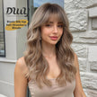 A photo of a smiling young woman wearing a long, wavy, strawberry-blonde DWY wig with full bangs. Text overlay on the beige background highlights 