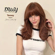 Model in a white ringer tee shows off a long, layered copper-red DWY wig with full bangs, styled with volume. Branded text reads 