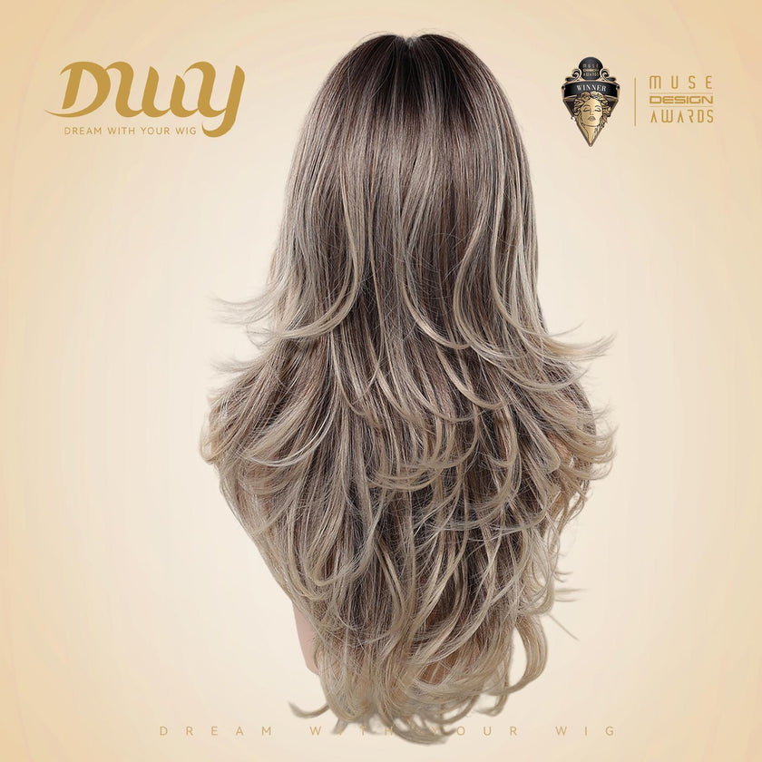 Back view of a mannequin head showcasing the DWY long, layered synthetic wig in highlighted brown and blonde. Background is beige with the gold DWY logo and Muse Design Awards badge.