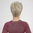 A back view photograph of a woman modeling a short, layered blonde pixie wig. The hair features dimensional blonde shades, blending highlights and lowlights for a natural look. The wig is styled with volume at the crown and tapers neatly at the nape of the neck, showing the distinct, textured layers. The woman is wearing a textured, shimmering burgundy long-sleeved top and small gold dangle earrings. The background is a plain, seamless light grey. The lighting is soft and even.