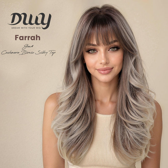 A woman with long, layered, ash-brown and blonde highlighted hair with bangs, wearing a beige top, models the DWY Farrah Gen4 synthetic wig against a beige background.