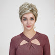 A studio portrait of a smiling woman against a grey background, modeling a short, layered blonde pixie wig.