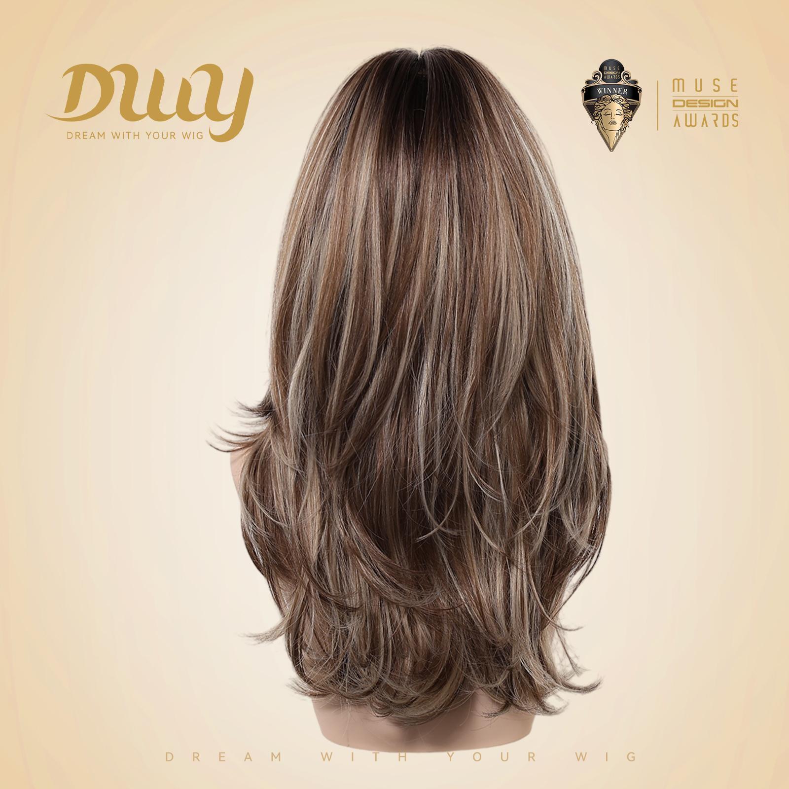A mannequin head viewed from the back, showcasing a long, layered DWY synthetic wig with brown and blonde highlights. The wig features a realistic dark root transition and textured ends. The background is a light beige studio setting with the gold DWY logo and a 'Muse Design Awards' emblem.