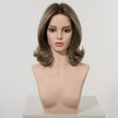 A front view of a realistic female mannequin head displaying a DWY wig. The medium-length, layered synthetic hair is a mix of dark brown and lighter ash brown highlights, styled with soft, flipped-out curls at the ends. A monofilament part is visible. The mannequin has neutral makeup. The background is a clean, plain studio white.