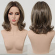 A mannequin head displays a medium-length, layered bob wig from DWY, featuring flipped ends. The front view shows the central part and face framing layers, while the back view highlights the stacked layers and volume. The wig has a natural dark brown root transitioning to a lighter ash brown balayage.