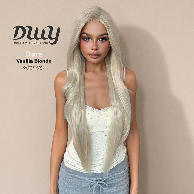 A woman models the DWY 'Dara' wig in a 'Vanilla Blonde' shade, featuring a monofilament part. This long, straight, light blonde hairpiece has subtle layering and a natural appearance. The model wears a cream lace-trimmed tank top and grey sweatpants. The background is a simple, solid beige wall with text overlay. There is a blue button on the chest of the model.
