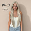 A woman models the DWY 'Dara' wig in a 'Vanilla Blonde' shade, featuring a monofilament part. This long, straight, light blonde hairpiece has subtle layering and a natural appearance. The model wears a cream lace-trimmed tank top and grey sweatpants. The background is a simple, solid beige wall with text overlay. There is a blue button on the chest of the model.