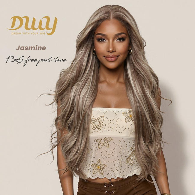 A woman models a long, wavy ash brown wig with blonde highlights from DWY Dream With Your Wig, styled in a 13x6 free part lace front. She wears an embroidered strapless top and brown pants against a beige background. The text 